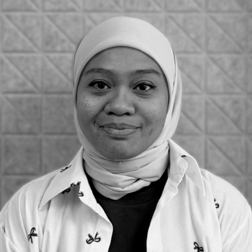 Close up portrait of a smiling woman wearing a light hijab and scarf against a brick patterned background